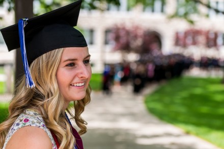 A female graduate sits in front of Conway Hall with her cap on