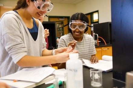 Two science students wearing goggles examine an object