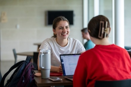 A girl smiles while sitting at a table in Arrupe Hall, sitting across from a fellow student