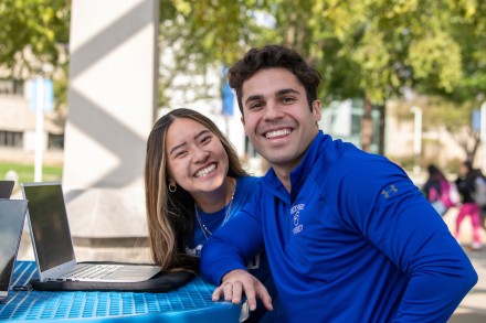A male and female student smile at the camera while studying on the pergola