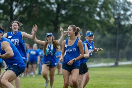 Group of students running and cheering, smiling, wearing Rockhurst apparel